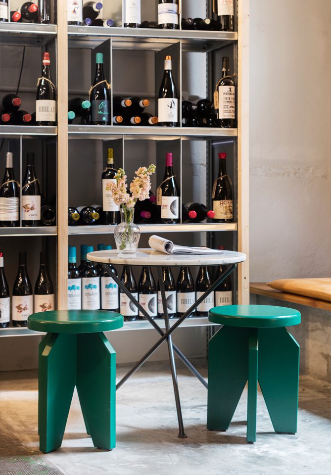 Racó d’Agüita wine specialist amb una taula, tamborets verds i ampolles de vi